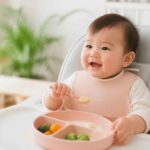 Uśmiechnięte niemowlę w krzesełku je posiłek z różowej miseczki podzielonej na przegródki